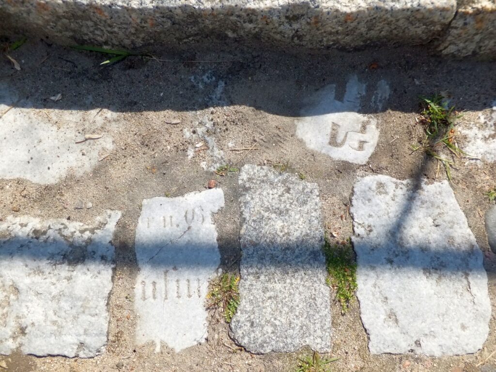 Fragmenty płyt nagrobnych wykorzystanych do budowy nawierzchni jezdni ulicy Południowej w Człopie – na górze widoczne znaki z alfabetu hebrajskiego, na dole niemiecka fraktura; lipiec 2015 roku; zbiory własne.