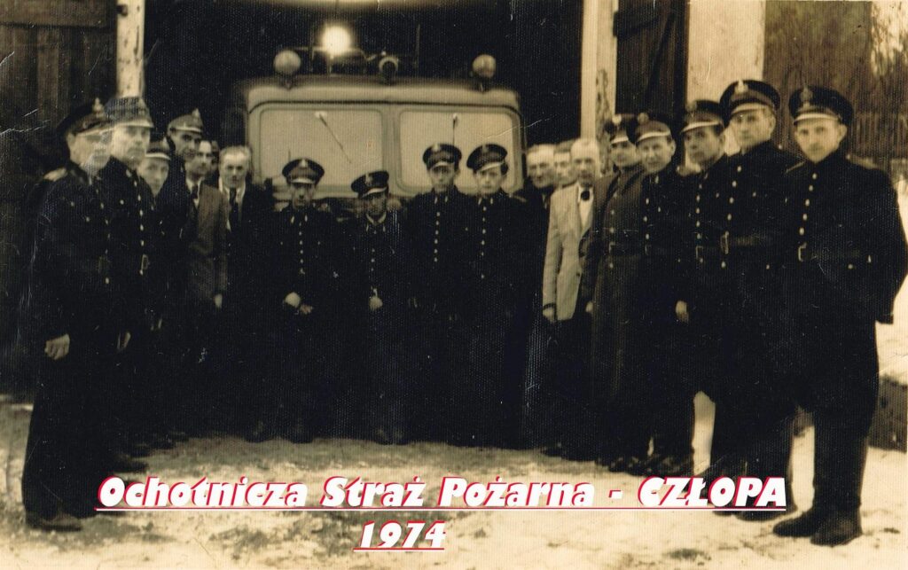Fotografia zbiorowa członków jednostki OSP Człopa przed ich pierwszą remizą przy skrzyżowaniu ulic Stanisława Moniuszki i Strzeleckiej. Jeżeli faktycznie jest to rok 1974, to oznacza, że to jej ostatnie chwile przed rozbiórką. Źródło fotografii: profil FB OSP Człopa, dostęp 3 maja 2026 roku – kliknij, aby przejść