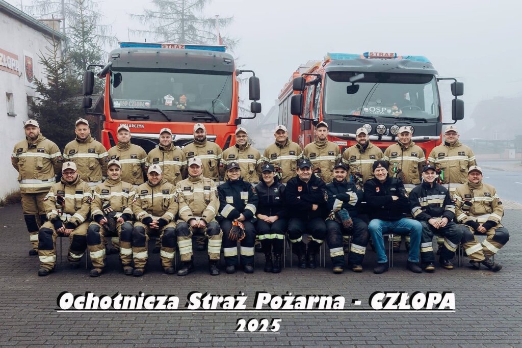Fotografia zbiorowa członków jednostki OSP Człopa na tle wozów MAN (numer rejestracyjny ZWA 17XX, numer operacyjny 579Z10) i Volvo (numer rejestracyjny ZWA 23G7, numer operacyjny 579Z12); remiza przy ulicy Ignacego Paderewskiego 9. Rok 2025. Źródło fotografii: profil FB OSP Człopa, dostęp 3 maja 2026 roku – kliknij, aby przejść